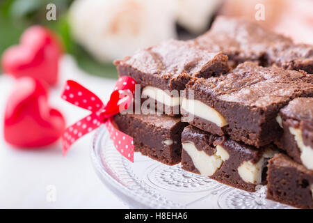 Valentinstag-Käsekuchen-Brownies auf Kuchen stehen auf rosa Rosen Hintergrund Stockfoto