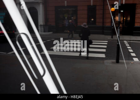 Eine Dame Fußgänger überquert einen Zebrastreifen mit den Streifen eines Apple iPhone im Fenster von John Lewis, London, England. Stockfoto