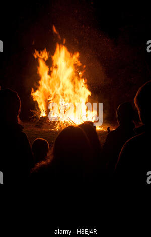 Dunkle gestalten beobachten der Flammen eines Lagerfeuers während der jährlichen 5. November Feuerwerk in Kington, Herefordshire, England Stockfoto