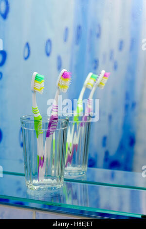 Zwei bunte Zahnbürsten in ein Glas vor dem Badezimmerspiegel mit Nebel bedeckt Stockfoto