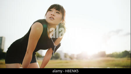 Junge sportliche Frau, die eine Pause von der Ausbildung. Chinesische Frauen stehen mit den Händen auf den Knien und wegsehen Morgen. Stockfoto