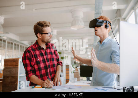Aufnahme von zwei jungen Männern, die virtual-Reality-Kopfhörer Tests. Unternehmer, VR-Brille und Kollegen schreiben von Notizen im Büro tragen. Stockfoto