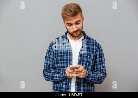 Verärgert bärtiger Mann SMS Nachricht auf Smartphone auf einem grauen Hintergrund isoliert Stockfoto