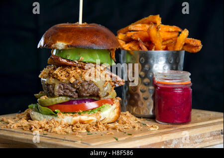 Beefburger und Brötchen mit Chips (Pommes) auf einem hölzernen Teller serviert. eine UK Stockfoto
