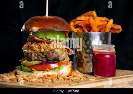 Beefburger und Brötchen mit Chips (Pommes) auf einem hölzernen Teller serviert. eine UK Stockfoto