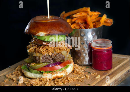 Beefburger und Brötchen mit Chips (Pommes) auf einem hölzernen Teller serviert. eine UK Stockfoto