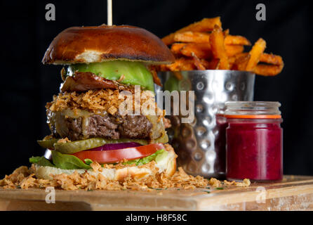 Beefburger und Brötchen mit Chips (Pommes) auf einem hölzernen Teller serviert. eine UK Stockfoto