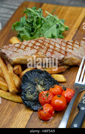 Steak & Chips mit Champignons und Tomaten auf einem hölzernen Teller serviert. eine UK-Essen-Küche Stockfoto