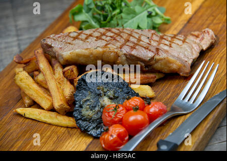 Steak & Chips mit Champignons und Tomaten auf einem hölzernen Teller serviert. eine UK-Essen-Küche Stockfoto