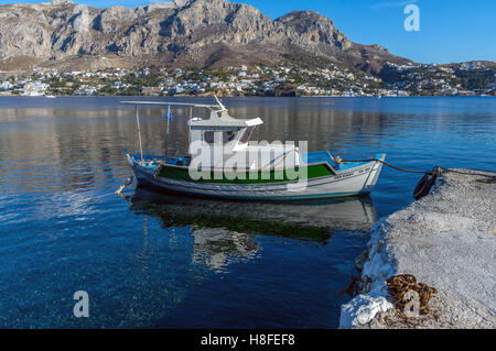 Kleine bunte Fischerboot, Telendos, Griechenland, mit felsigen Inseln hinter Stockfoto