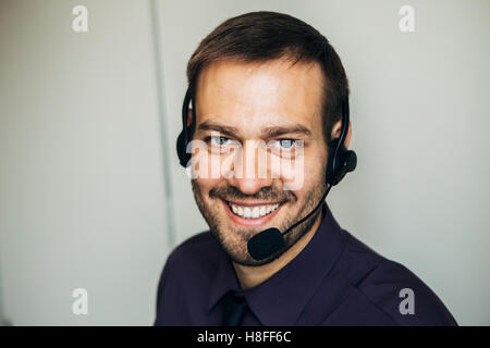 Porträt von hübschen jungen männlichen Betreiber in Kopfhörer Blick in die Kamera und lächelnd stehend vor weißem Hintergrund Stockfoto