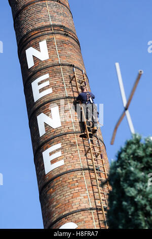 Kirchturm-Buchsen arbeiten auf einem sehr hohen Schornstein an einem sonnigen Tag Stockfoto