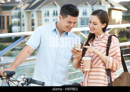 Junges Paar betrachten Telefon unterwegs zur Arbeit im städtischen Umfeld Stockfoto