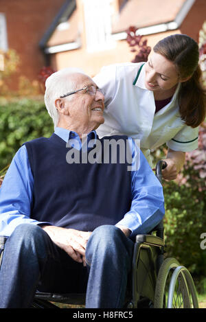 Pflegeperson Senior Mann im Rollstuhl schieben Stockfoto