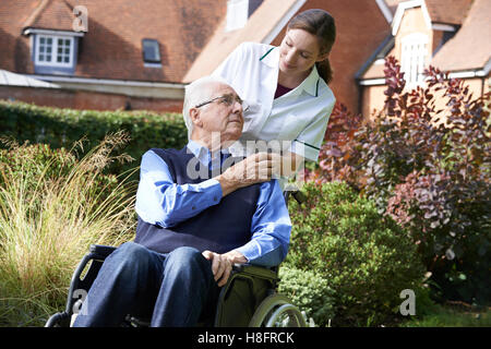Pflegeperson Senior Mann im Rollstuhl schieben Stockfoto