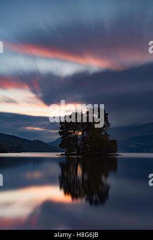 Loch Tay, Perthshire, Schottland, reflektiert das Licht von der untergehenden Sonne, wie es geht hinter den Bäumen auf einer der Inseln. Stockfoto