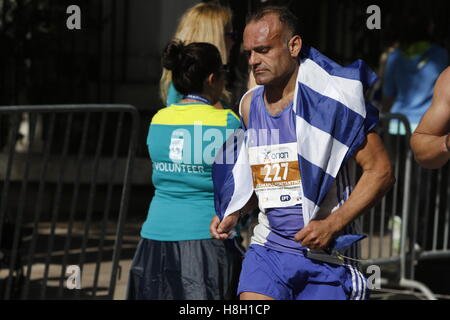 Athen, Griechenland. 13. November 2016. Ein Läufer ist eingehüllt in eine griechische Flagge. Tausende von Menschen aus der ganzen Welt nahmen an 2016 Athen Marathon authentisch, die in der Stadt von Marathon beginnt und endet in Athen, die Route, die der Legende nach zuerst von den griechischen Boten Pheidippides 490 v. Chr. betrieben wurde. Stockfoto