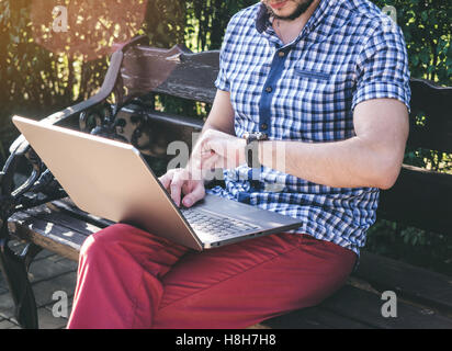 Junger Mann im Hemd tragen sieht auf seine Uhr und arbeiten auf seinem Laptop, modernes Design notebook Stockfoto