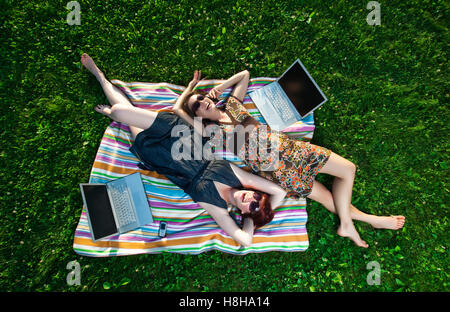 Zwei junge Frauen mit Laptop und Handy-Verlegung auf einer Decke in der Wiese Stockfoto