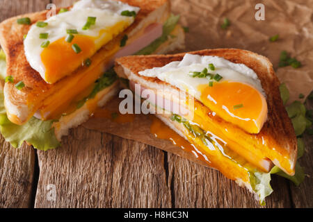 Schneiden Sie Sandwich mit gebratenem Ei, Schinken und Käse-close-up auf dem Papier auf dem Tisch. horizontale Stockfoto