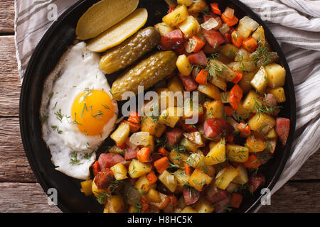 Skandinavische Bratkartoffeln mit Würstchen, Eiern und Gurken Nahaufnahme auf einer Platte. horizontale Ansicht von oben Stockfoto