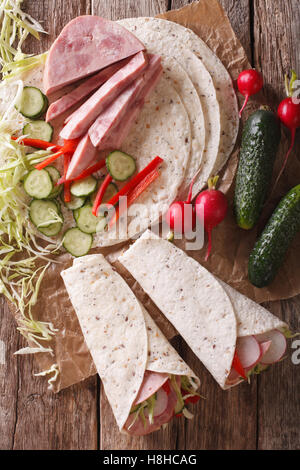 Sandwich Brötchen mit Schinken, Käse und frischem Gemüse Nahaufnahme und Zutaten auf den Tisch. vertikale Ansicht von oben Stockfoto