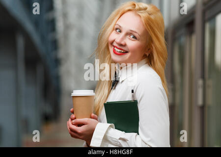 Lächelnd Ingwer mit Buch und Kaffee in der Hand im Gebäude Stockfoto