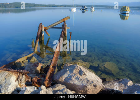 Tranquill Szene Bucht am Morgen mit einem alten, rostigen Pier im Vordergrund und verankerte Boote im Hintergrund Stockfoto