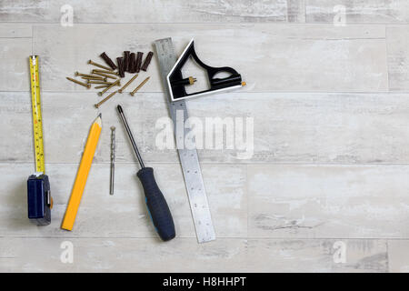 Maßband, Bleistift, Bohrer, Geodreieck, Schraubendreher, Schrauben und Dübel liegen auf einer Etage shabby Stil Stockfoto