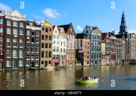 Ein Ausflugsboot Motoren zusammen vor der berühmten Häuser säumen den Rand der Damrak Canal Basin, Amsterdam, Niederlande Stockfoto