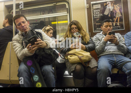 U-Bahn-Fahrer benutzen ihre Handys, auf dem Heimweg von der Arbeit in den Feierabendverkehr in Brooklyn, New York. Stockfoto