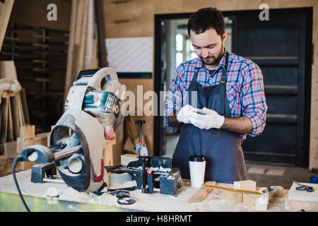 Tischler SMS jemand auf seinem Smartphone in der Nähe von Kreissäge in einem staubigen workshop Stockfoto