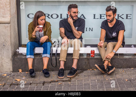 Drei spanische Freunde, ein Weibchen und zwei Männchen, sitzen vor einem Shop Schaufenster trinken Kaffee und alkoholfreie Getränke während der th Stockfoto