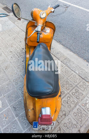 Eine sehr alte orange und schwarz Vespa Super Motorscooter parkt auf einem Bürgersteig in Barcelona, Spanien. Stockfoto