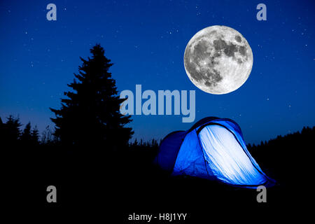 Super-Mond. Blau beleuchteten Zelt mit Reisenden in den Bergen. Hintergrund eine Kiefer Baum Silhouette und der Sternenhimmel Sommer nig Stockfoto