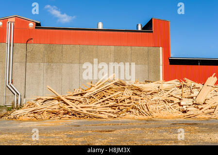 Hölzerne Trümmerhaufen vor roten Industriegebäude. Das Holz ist Abfall aus dem Sägewerk und zu Hackschnitzel erfolgt eine Stockfoto