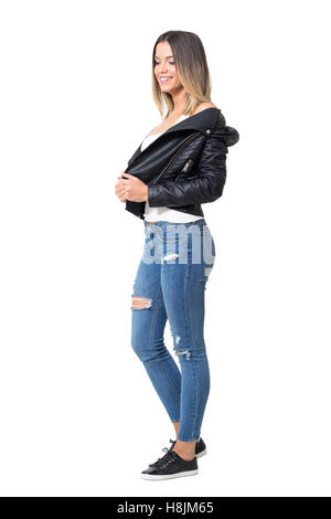 Ziemlich Lächeln schüchtern casual Mädchen tragen Lederjacke, zerrissene Jeans und schwarze Turnschuhe blickte. Ganzkörper-Länge isoliert Stockfoto