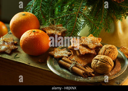 Mandarinen und Platte mit Ingwer Cookies, Zimtstangen, Walnüsse auf Fichte Zweige Hintergrund Stockfoto