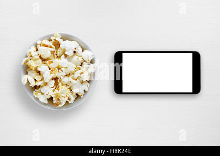 Popcorn und Smartphone auf weißen Tisch Stockfoto