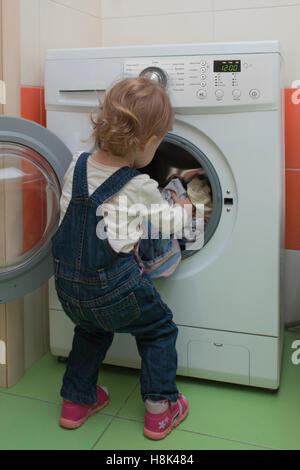 kleines Kind bringt Wäsche in die Waschmaschine. Mutters Helfer. 2 Jahre alt. Stockfoto