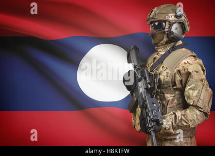 Soldat im Helm holding Maschinengewehr mit Nationalflagge auf Hintergrund - Laos Stockfoto