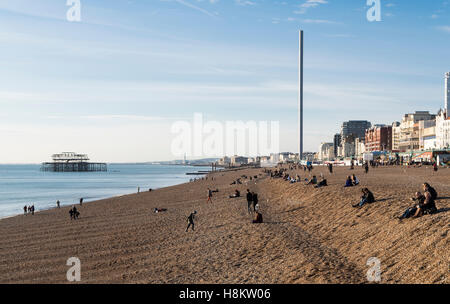 Blick auf Brighton Beach, mit Blick auf den Pier West und i360 mit Menschen genießen Sonnenschein sitzt auf Steinen und Kies Stockfoto