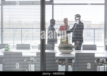 Geschäftsleute Händeschütteln von weiblichen Kollegen im Sitzungsraum durch Jalousie Fenster gesehen Stockfoto