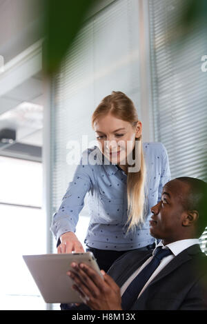 Junge Frau, die etwas auf digital-Tablette an männlichen Kollegen im Büro Stockfoto