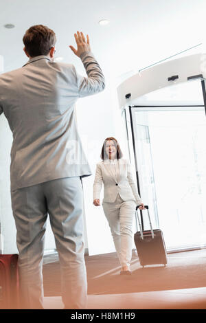 Fröhliche Geschäftsfrau mit Gepäck zu Fuß in Richtung männlicher Kollege im Convention center Stockfoto