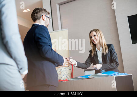 Angestellte an der Rezeption geben Personalausweis zum Geschäftsmann im Convention center Stockfoto