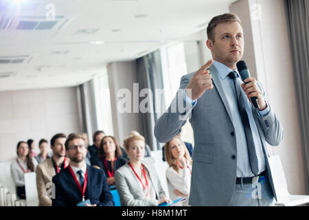 Geschäftsmann zeigt während des Sprechens über Mikrofon Seminar im Convention center Stockfoto