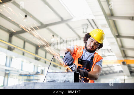 Junge Arbeiter mit Schleifer auf Metall in Fabrik Stockfoto