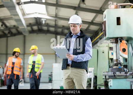 Ältere männliche Inspektor schreiben in Zwischenablage beim Arbeitnehmer im Hintergrund bei industry Stockfoto