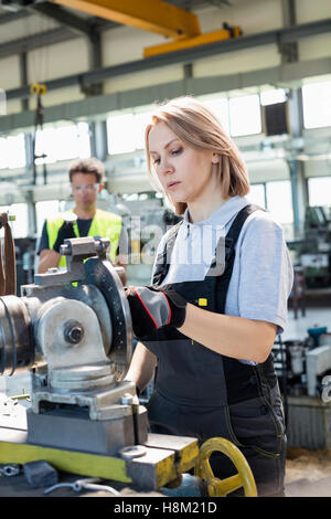 Ältere Arbeitnehmerin arbeiten an Maschinen mit Kollegen im Hintergrund im Werk Stockfoto